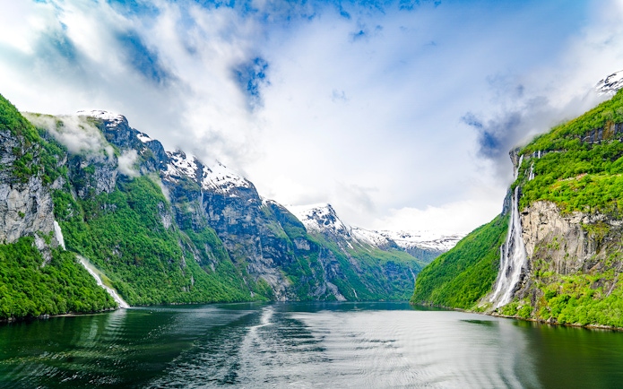Geirangerfjord in Norway with waterfalls cascading down lush green cliffs.