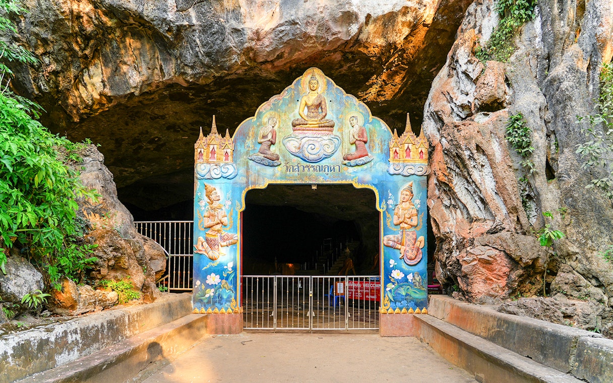 Entrance to a decorated cave temple in Phuket, featuring colorful religious artwork.