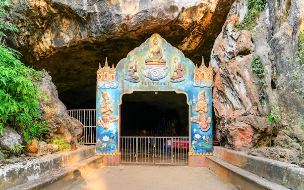 Entrance to a decorated cave temple in Phuket, featuring colorful religious artwork.