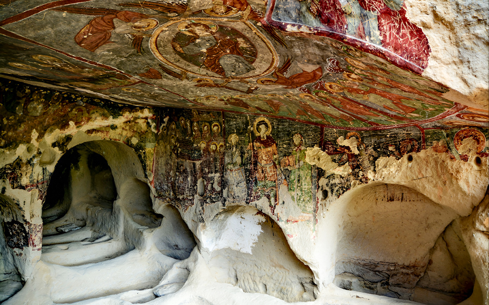 Underground cave church with fresco paintings on walls and ceiling.