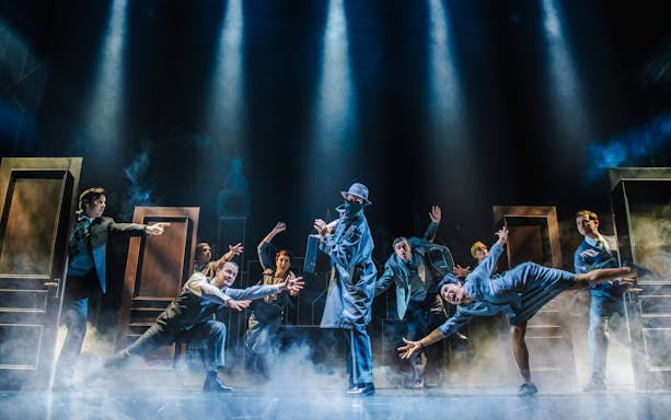 Actors performing a comedic spy scene on stage with dramatic lighting.