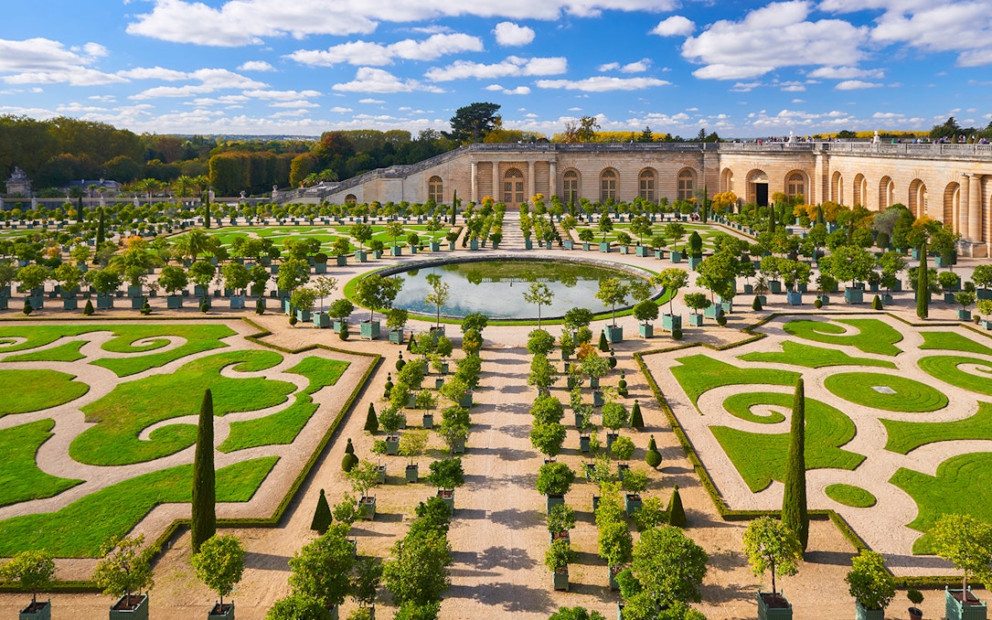 Versailles Palace gardens with tourists exploring the landscaped courtyard, France.