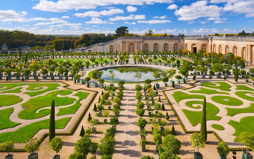 Versailles Palace gardens with tourists exploring the landscaped courtyard, France.