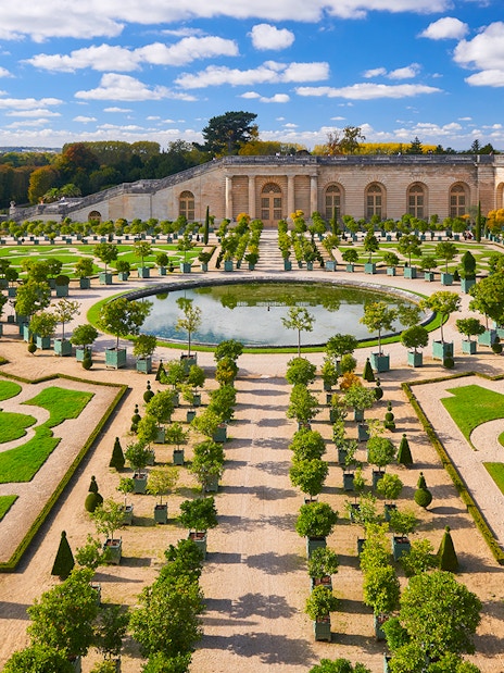Versailles Palace gardens with tourists exploring the landscaped courtyard, France.