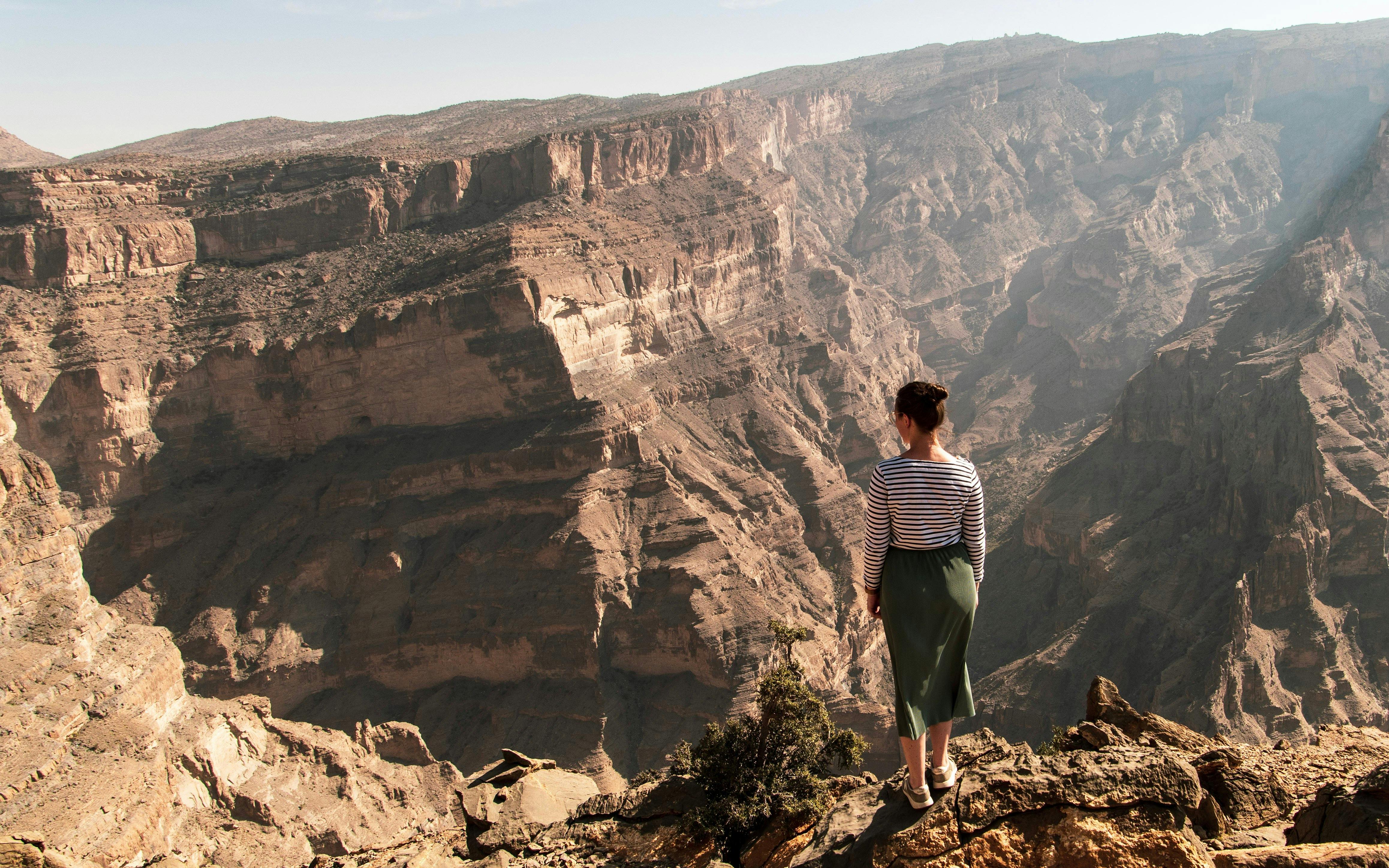Person standing on cliff edge overlooking Jebel Akhdar mountains in Oman.
