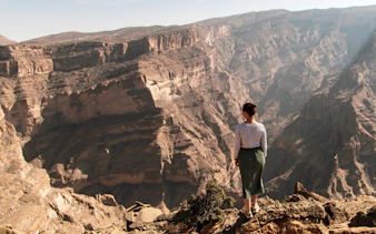 Person standing on cliff edge overlooking Jebel Akhdar mountains in Oman.