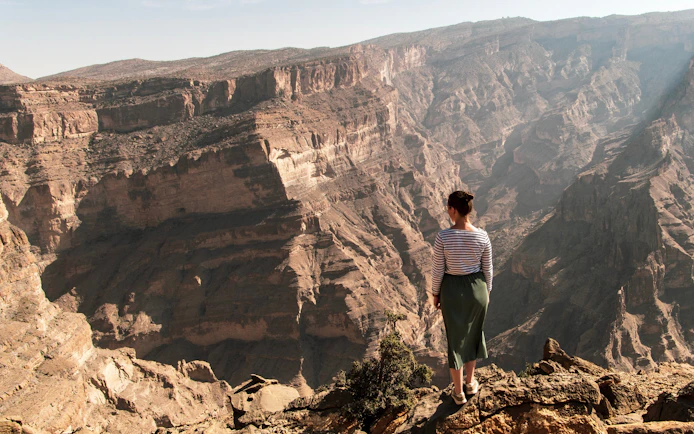 Person standing on cliff edge overlooking Jebel Akhdar mountains in Oman.