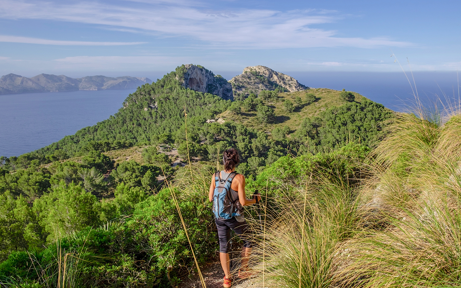 A man in blue tshirt hiking in the Sa Talaia region, surrounded by shrubs and a cliff