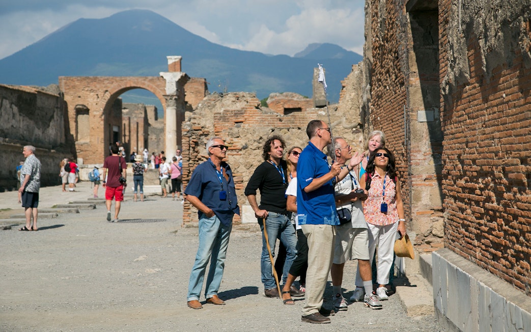 Visitors with a guide exploring ancient ruins in Pompeii with Mount Vesuvius in the background.