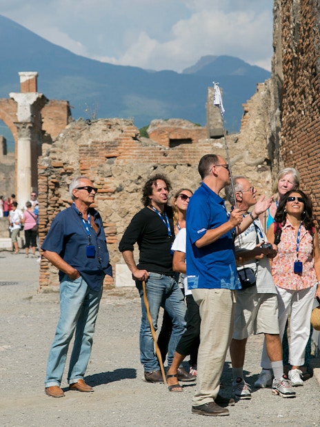 Visitors with a guide exploring ancient ruins in Pompeii with Mount Vesuvius in the background.