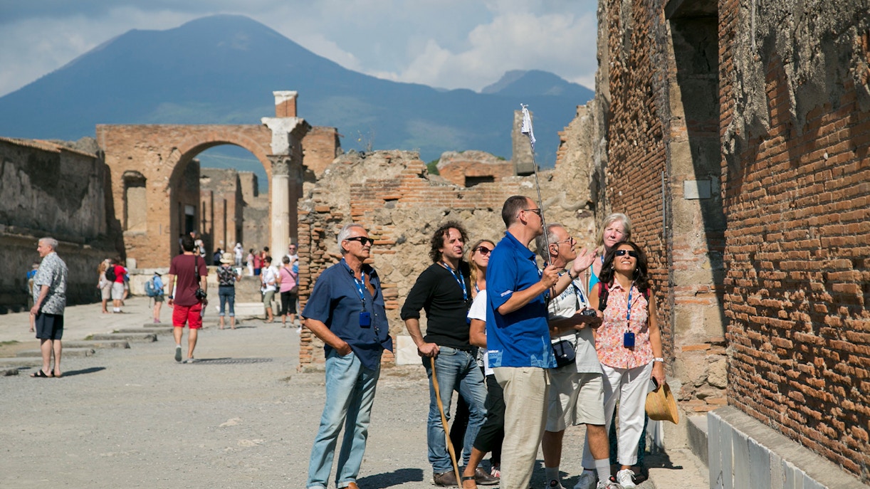 Visitors exploring ancient ruins with a guide in Pompeii, Italy, on a day trip.