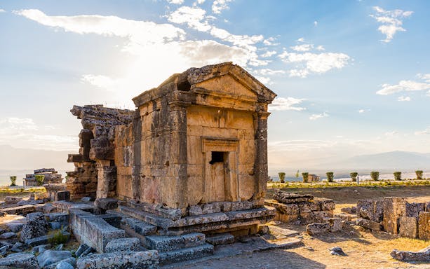 Ancient stone tomb in Hierapolis, Pamukkale, with scenic landscape in the background.