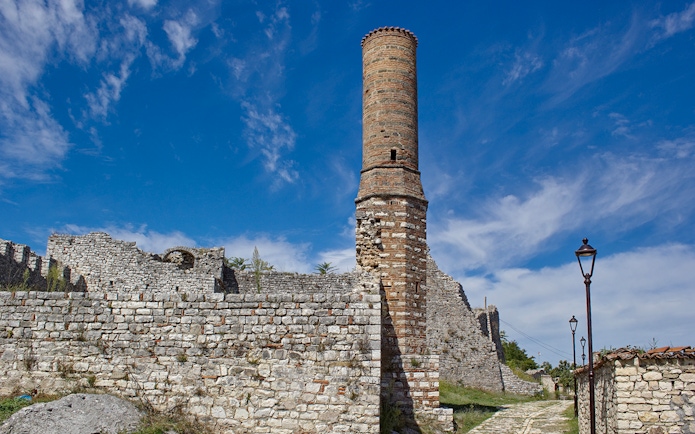 Old mosque minaret at Berat Fortress, Albania, with stone walls and pathway.