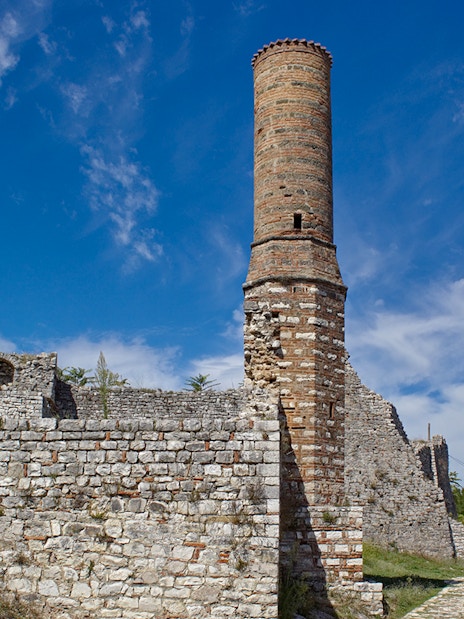 Old mosque minaret at Berat Fortress, Albania, with stone walls and pathway.