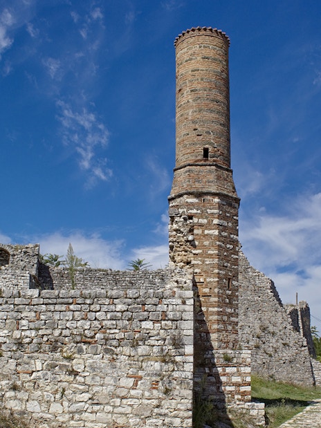 Old mosque minaret at Berat Fortress, Albania, with stone walls and pathway.