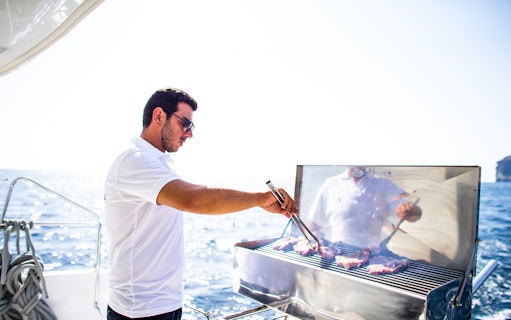 Man grilling meat on a yacht during a Semi Private Comfort Day Cruise.