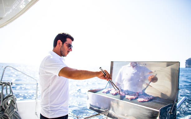 Man grilling meat on a yacht during a Semi Private Comfort Day Cruise.