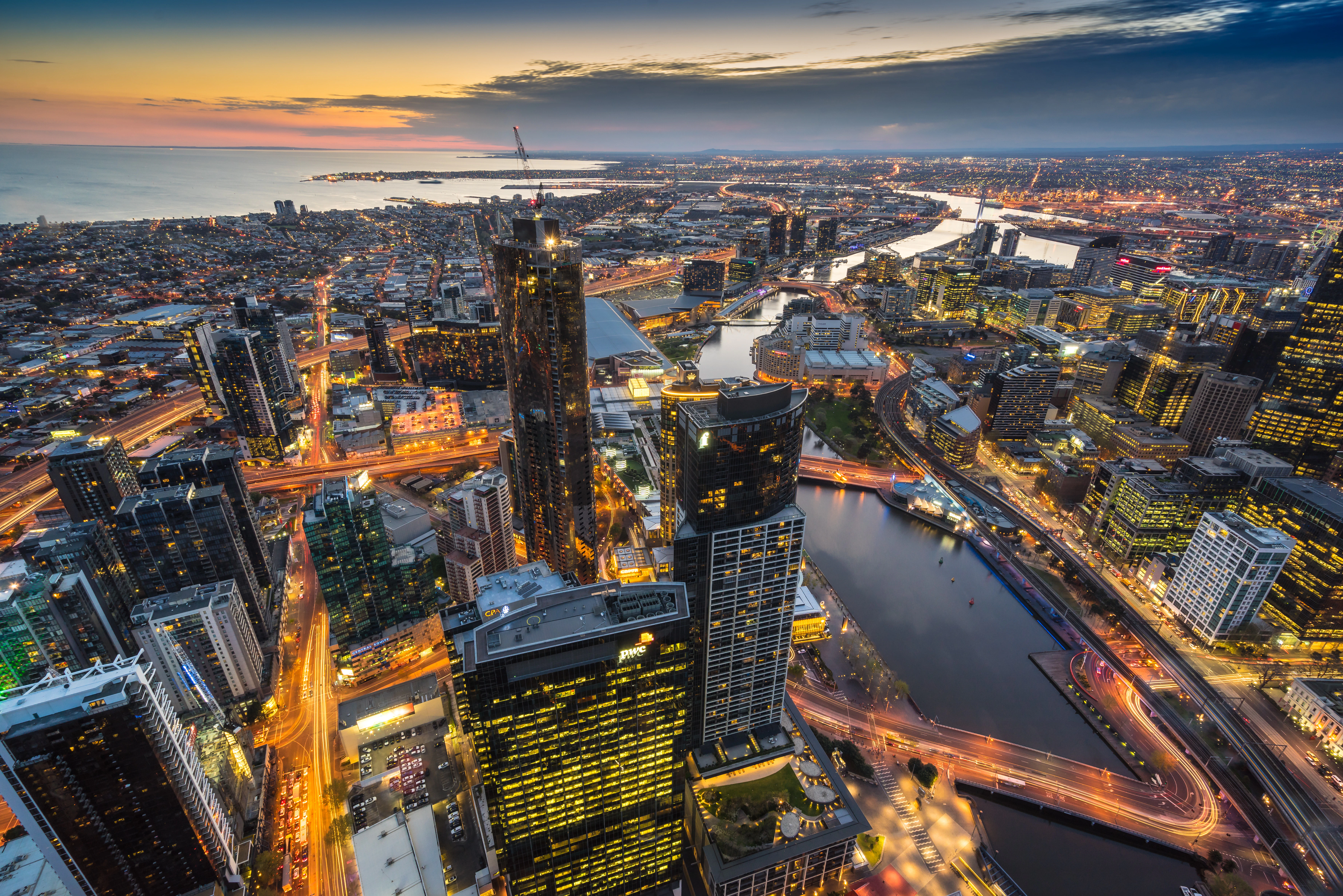 Melbourne skyline with Yarra River at evening, city lights reflecting on water.