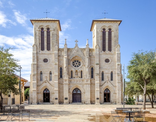 San Fernando Cathedral facade in San Antonio, Texas, with trees and seating in the foreground.