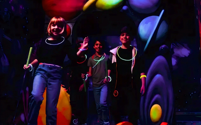 Guests playing Blacklight Mini Golf with glowing accessories and space-themed decor.
