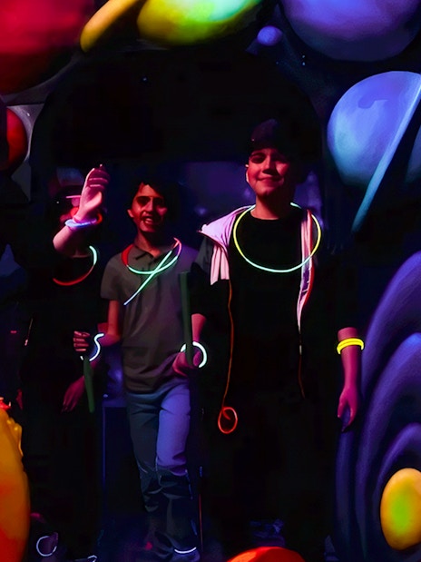 Guests playing Blacklight Mini Golf with glowing accessories and space-themed decor.