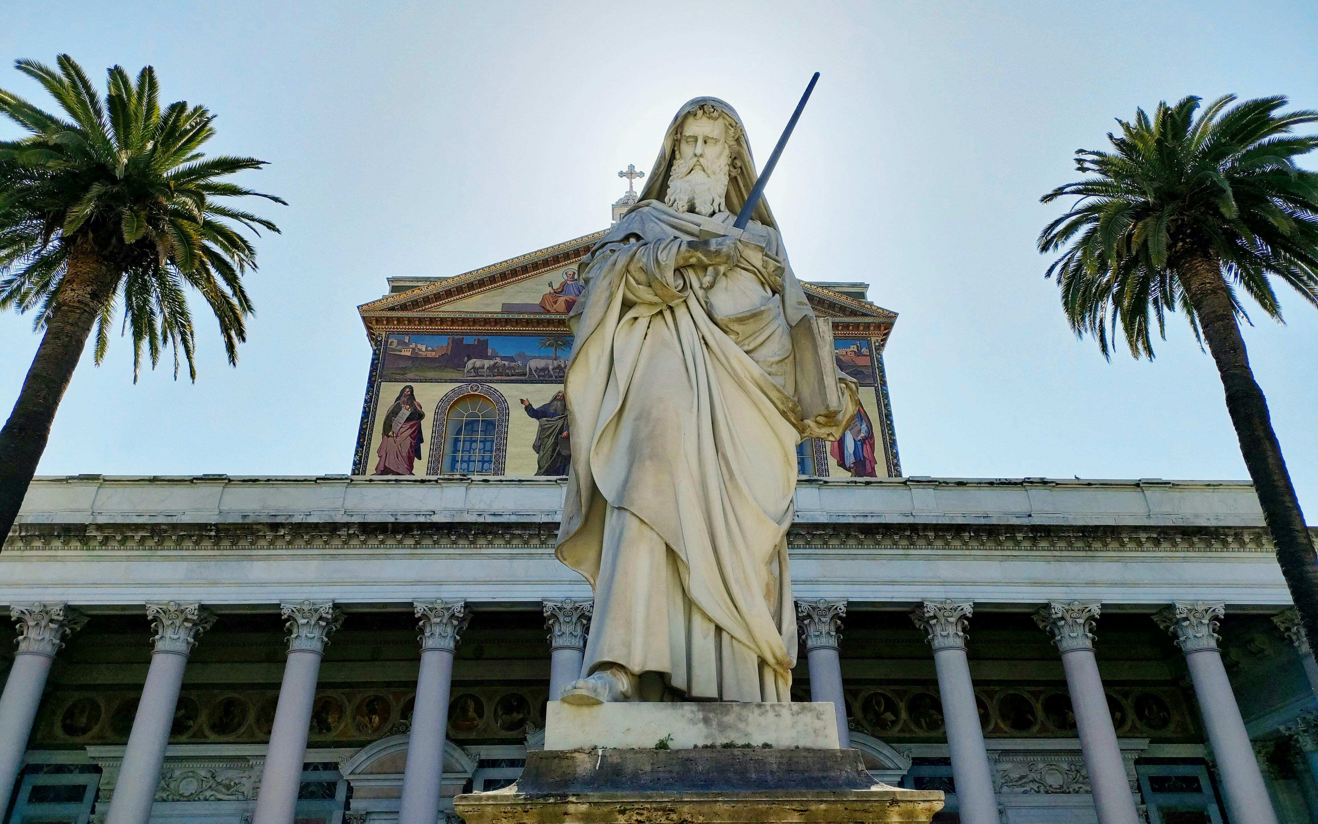 Colossal statue of Saint Paul at the Papal Basilica, Rome, flanked by palm trees.