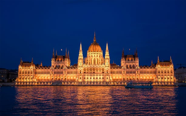 Hungarian Parliament illuminated at night viewed from a Danube River sightseeing cruise in Budapest.