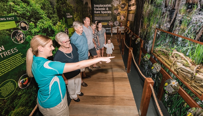 Visitors touring Cairns Aquarium exhibit with guide pointing at display.