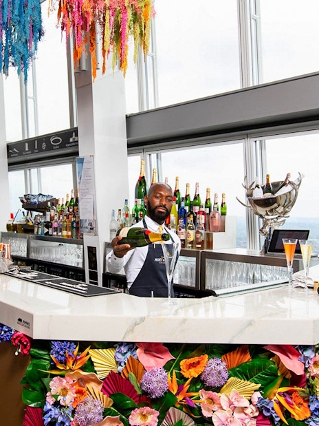 Bartender serving champagne at The Shard's bar with city view in London.