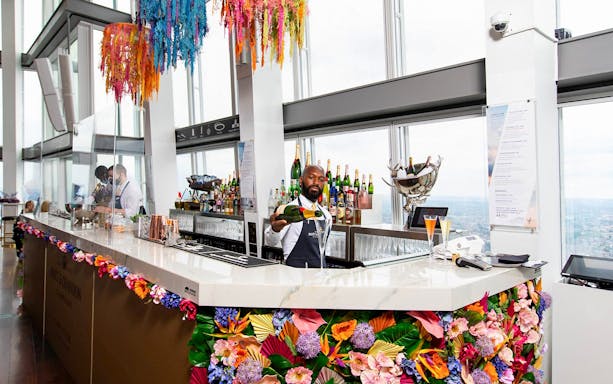 Bartender serving champagne at The Shard's bar with city view in London.