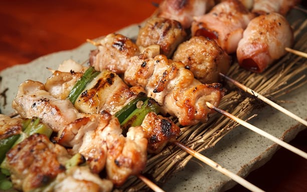 Grilled yakitori skewers with chicken and vegetables on a ceramic plate.