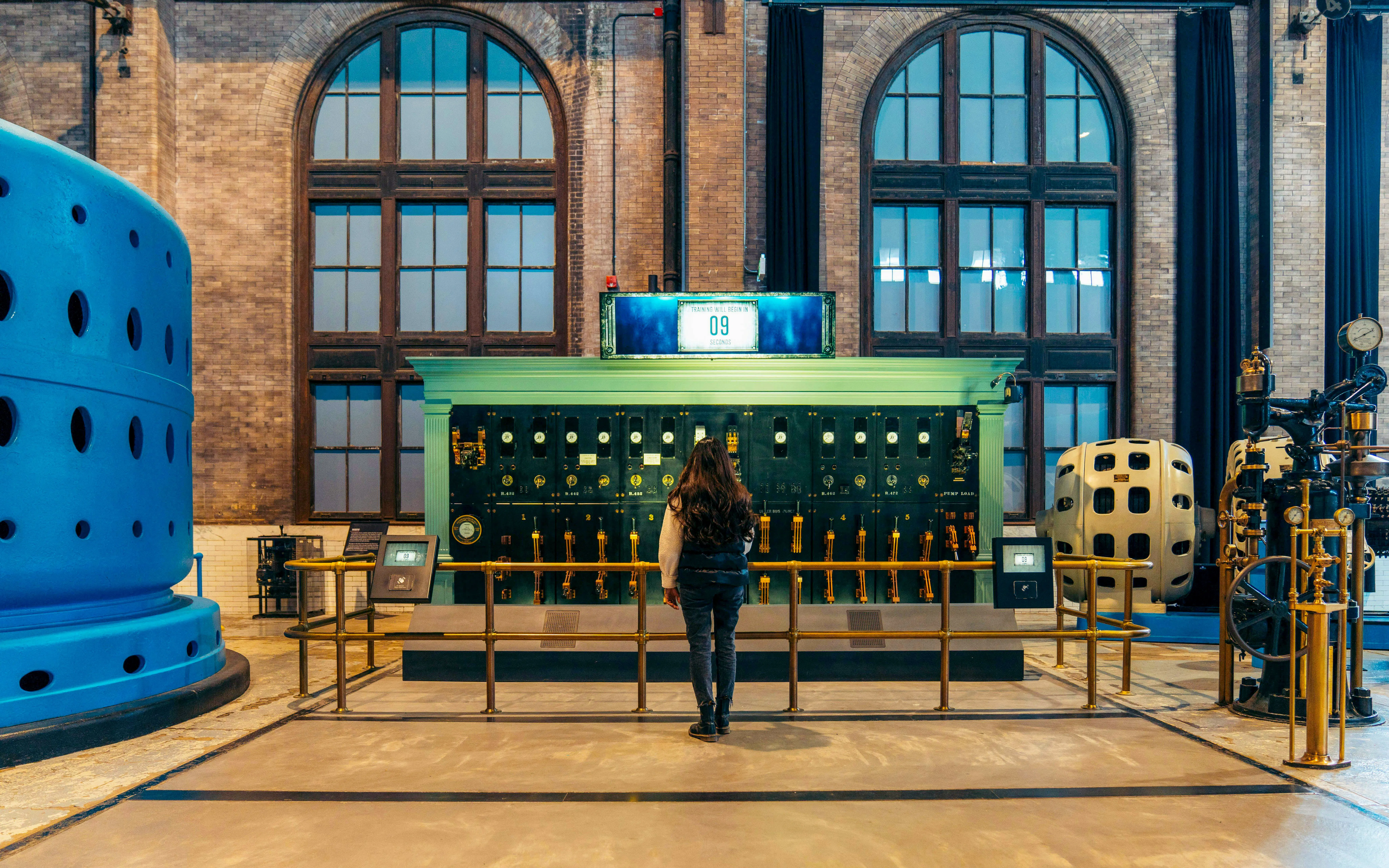 Visitor observing a historic generator control panel in an industrial museum.