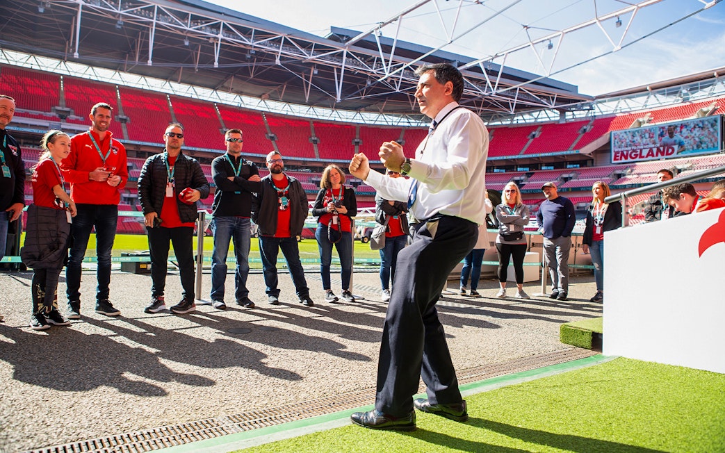 Tour group at Wembley Stadium, London, with guide explaining features.