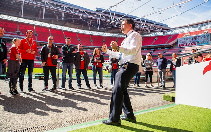 Tour group at Wembley Stadium, London, with guide explaining features.