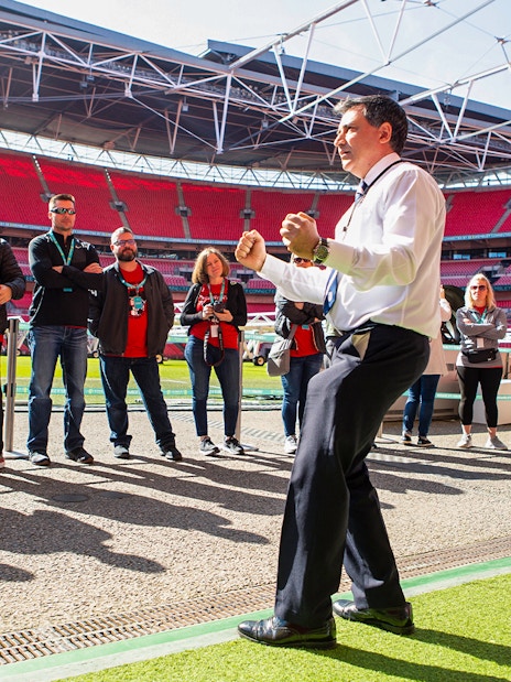 Tour group at Wembley Stadium, London, with guide explaining features.