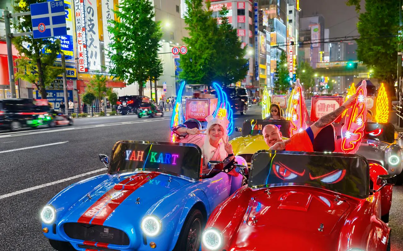 Go-kart tour participants in costume driving through illuminated Tokyo streets at night.