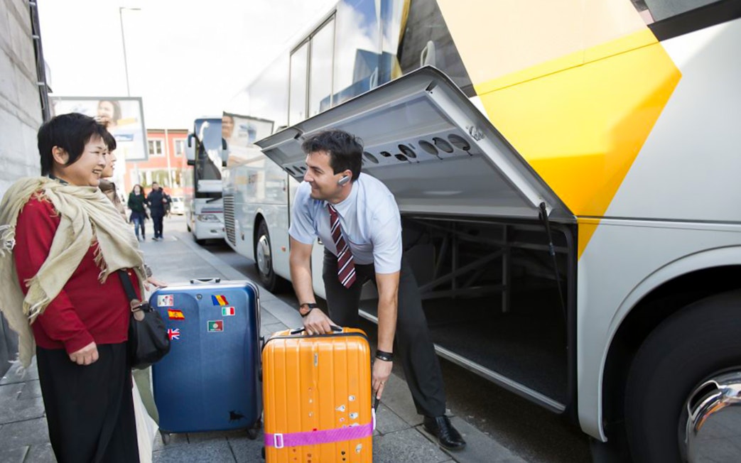 Staff assisting passenger with luggage at a bus terminal.