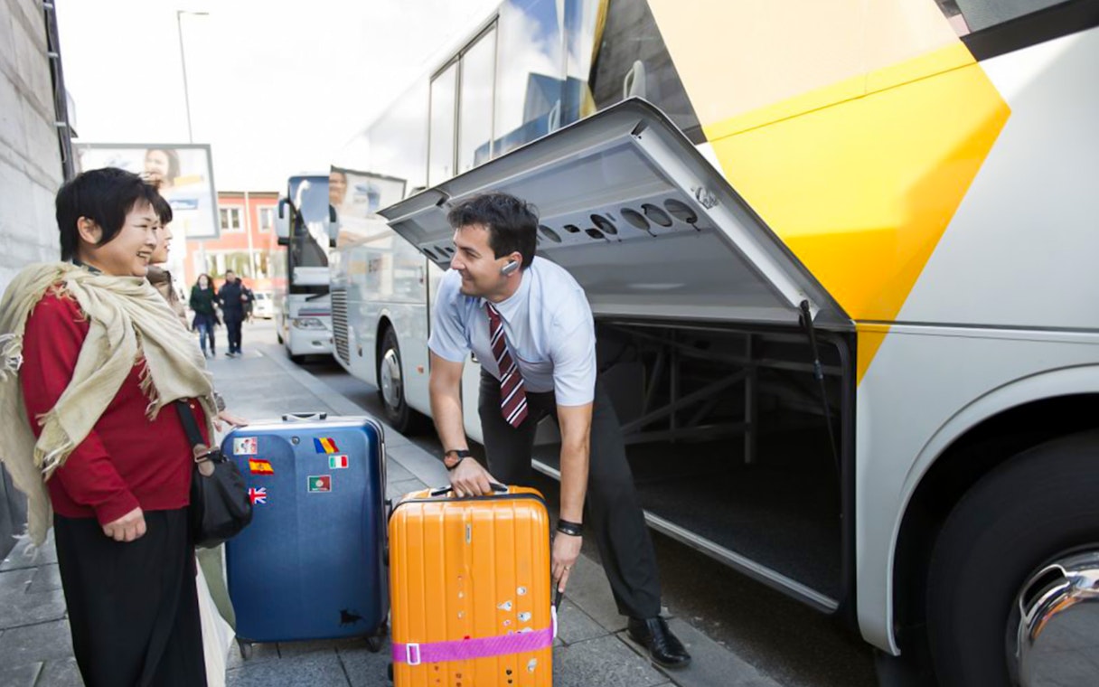 Staff assisting passenger with luggage at a bus terminal.