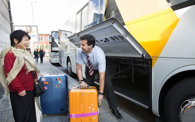 Staff assisting passenger with luggage at a bus terminal.