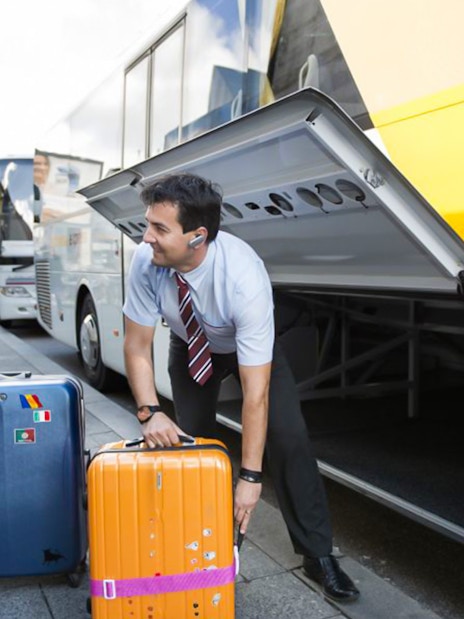 Staff assisting passenger with luggage at a bus terminal.