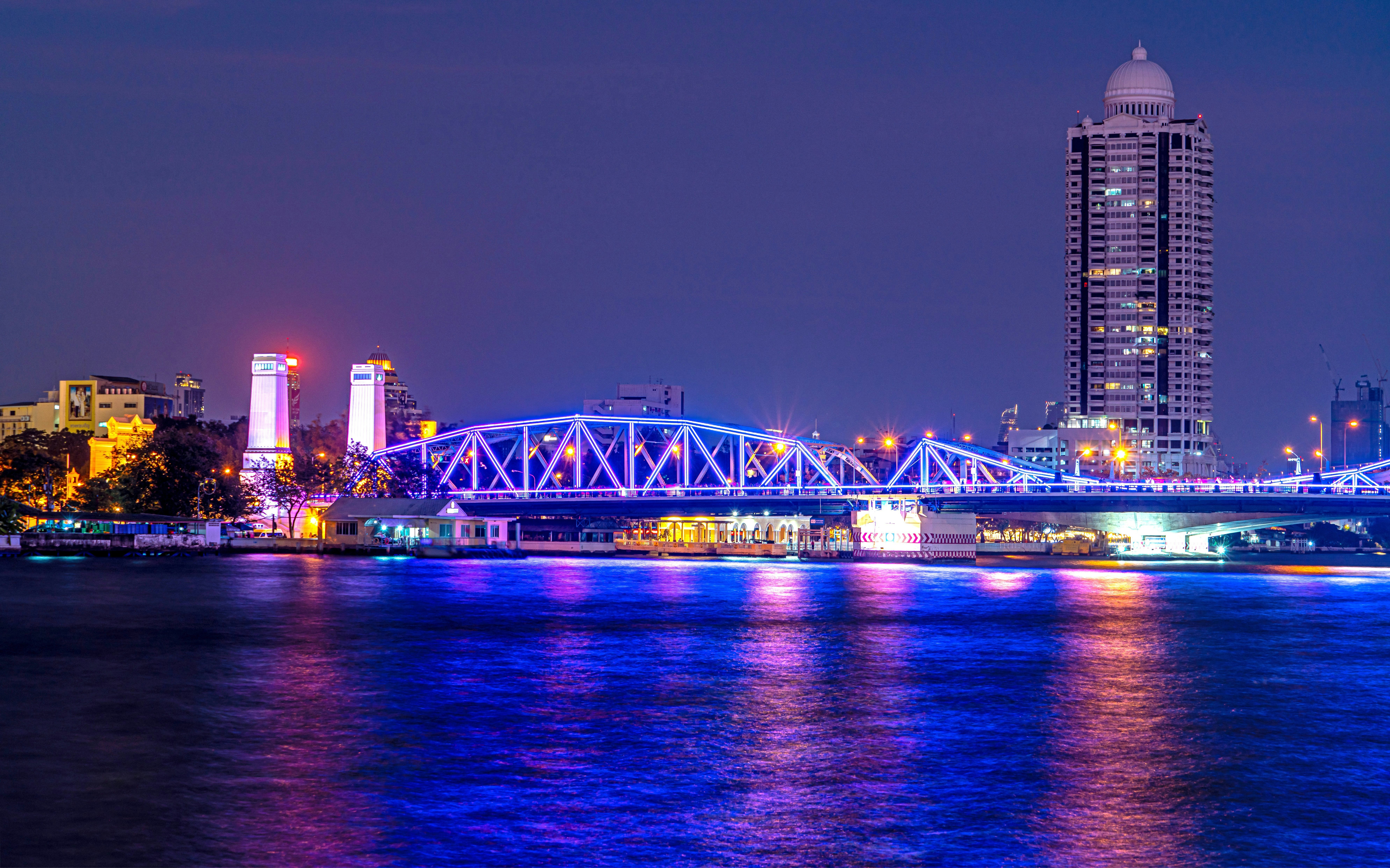 Saphan Phut Memorial Bridge illuminated at night with city skyline in Bangkok.