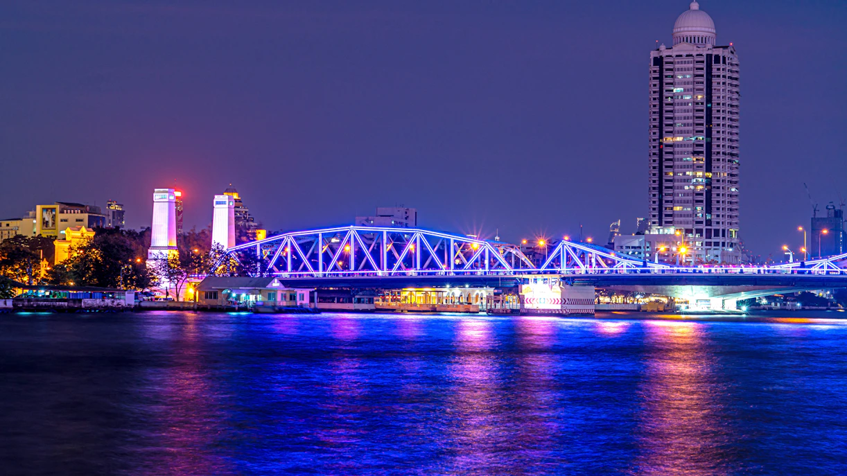 Saphan Phut Memorial Bridge illuminated at night with city skyline in Bangkok.
