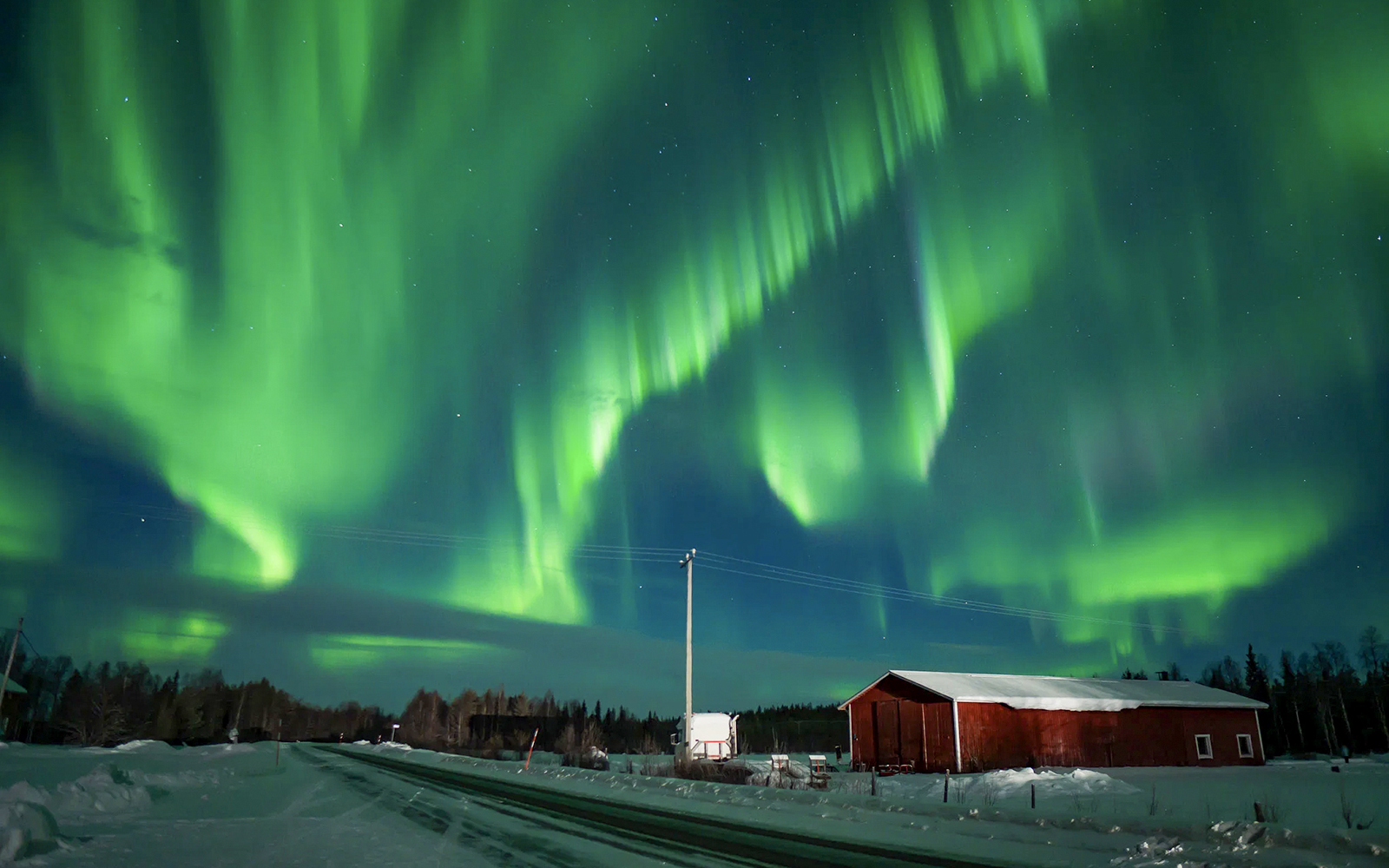Northern Lights over snowy landscape with red cabin during tour.
