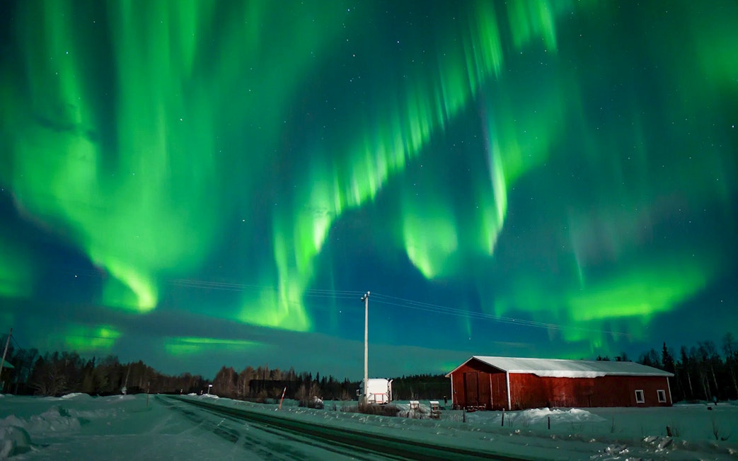 Northern Lights over snowy landscape with red cabin during tour.
