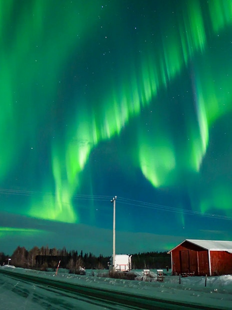 Northern Lights over snowy landscape with red cabin during tour.