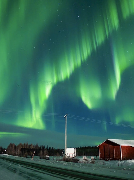 Northern Lights over snowy landscape with red cabin during tour.