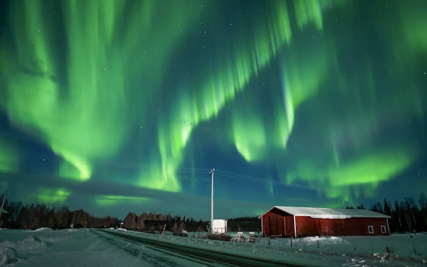 Northern Lights over snowy landscape with red cabin during tour.