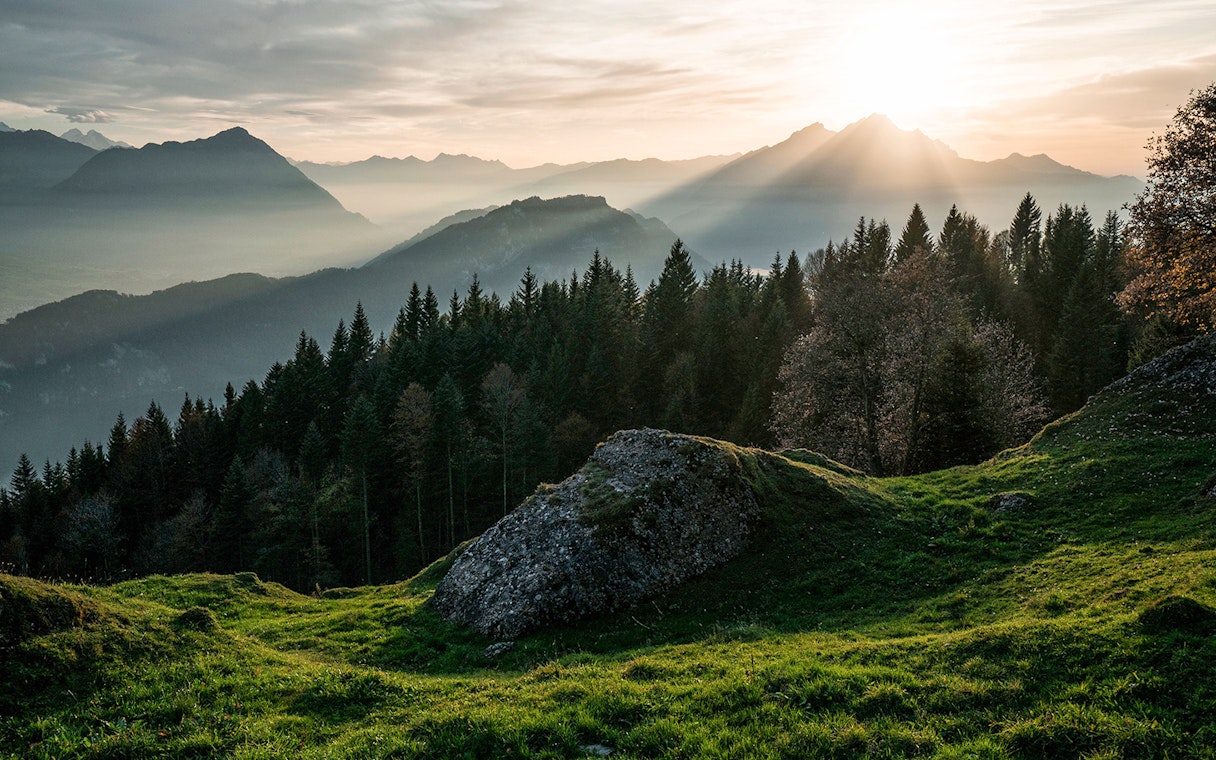 Mount Rigi landscape with sun rays over forested hills and distant mountains.