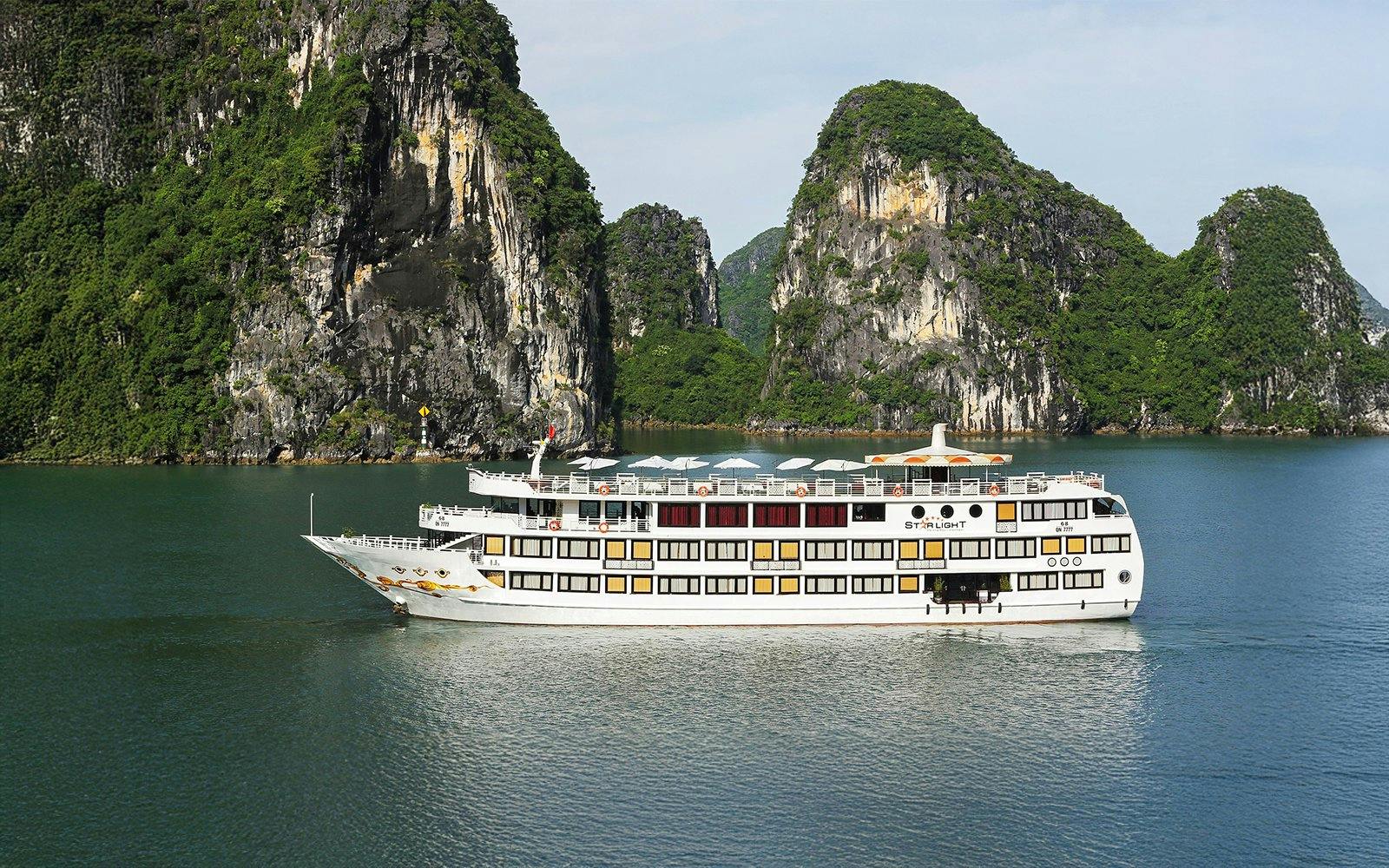 Starlight Cruise sailing in Halong Bay with limestone cliffs in the background.