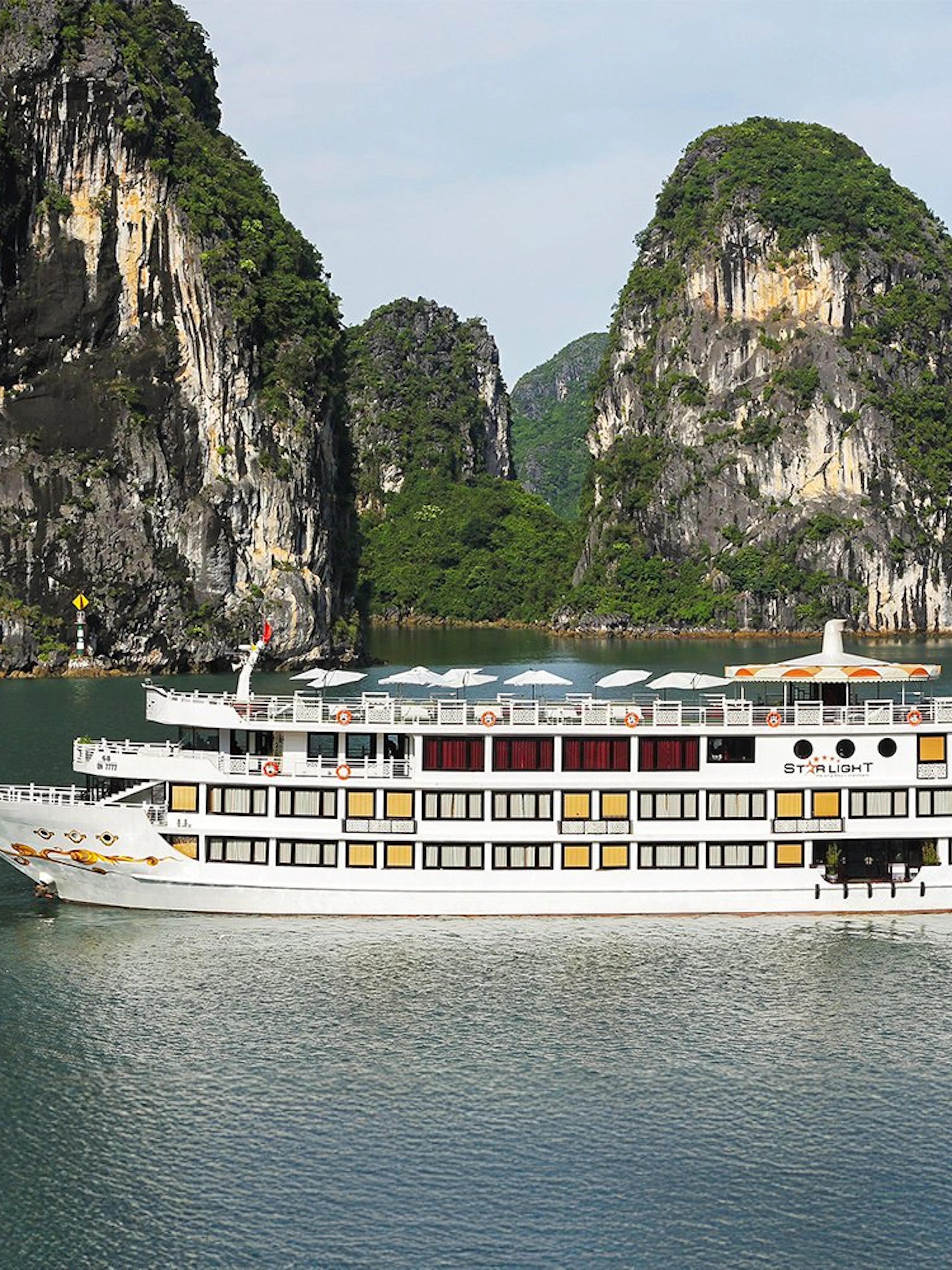 Starlight Cruise sailing in Halong Bay with limestone cliffs in the background.